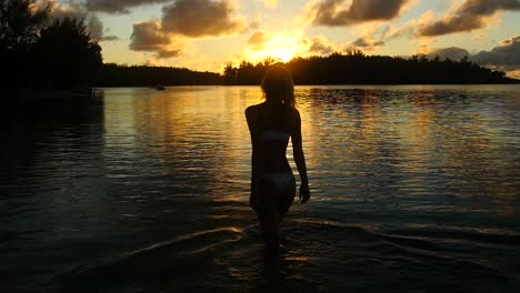 Silhouette-Einer-Frau,-Die-Bei-Sonnenuntergang-In-Französisch-Polynesien-Im-Wasser-Spaziert